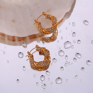 Close-up of golden twisted hoop earrings with white zircon on a reflective water surface