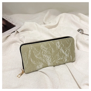 Detail of a dusty green velvet textured long wallet with gold zipper on white fabric