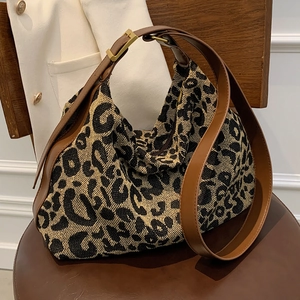 Large leopard print hobo bag with brown leather strap displayed on a leather chair