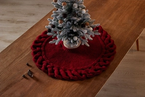Close-up of red cable knit mini Christmas tree skirt on dark wooden table with festive tree