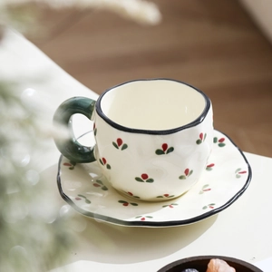 Close-up of beige ceramic coffee cup with hand-painted red flower buds and green leaves