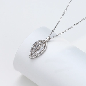 Detail of leaf pendant with pave-set zircons on silver chain over white pedestal