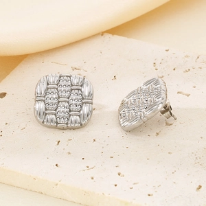 Close-up of silver square stud earrings with woven texture and dotted metal details