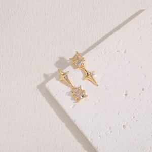 Detail view of gold earrings with star and square zircon elements on a textured stone