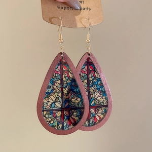 Close-up of ethnic teardrop wooden earrings with colorful floral patterns and gold hooks