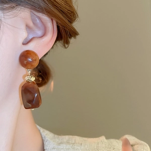Close-up of caramel resin irregular geometric earrings with golden metal link worn by model