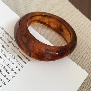 Detailed view of thick amber resin bangle with tortoiseshell texture on vintage book page