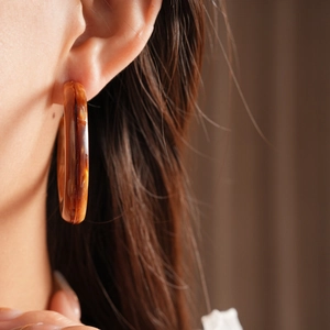 Close-up of model wearing a C-shaped amber resin earring with marbled texture