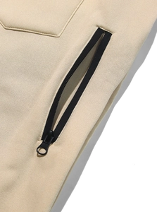 Dettaglio della tasca con cerniera e tessuto in pile sui pantaloni sportivi beige