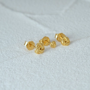 Macro shot of three gold-plated silver twisted knot stud earrings on white stone background
