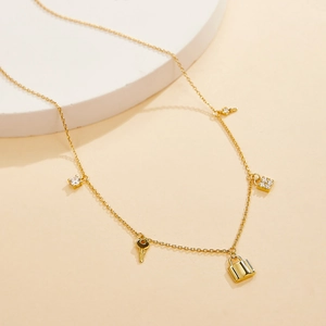 Close-up of golden S925 silver necklace with sparkling zircon key and lock charms