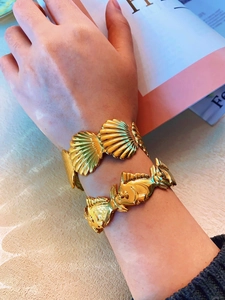 Detailed close-up of gold scallop and fish link bracelets with high-polish metallic finish