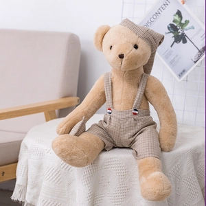 Cute teddy bear plush in brown plaid overalls and matching sleep cap on a sofa