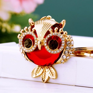 Detailed close-up of a golden owl keychain with a large red gemstone and crystal rhinestones
