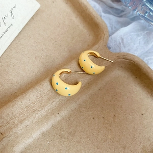 Macro shot of yellow C-shaped hoop earrings with blue polka dots on a pulp tray