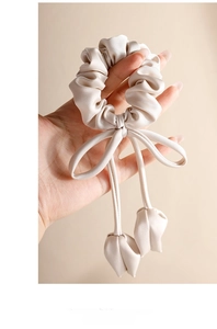 Detailed view of a beige silk bow scrunchie with long ribbons and 3D tulip accents