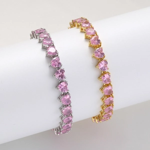 Detail of gold and silver bracelets featuring pink heart-shaped gemstones on white prop