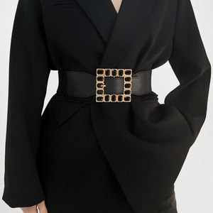 Detail of a wide black elastic waist belt with a gold square buckle featuring black stones