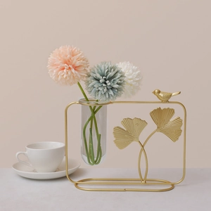 Golden ginkgo leaf metal vase stand with glass tube and bird detail on a beige desktop