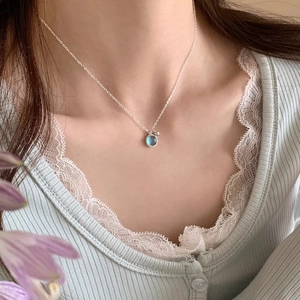 Close-up of minimalist silver necklace with round light blue gemstone pendant on model