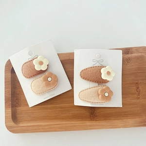 Detailed view of felt flower hair clips in milk tea colors on a wooden tray