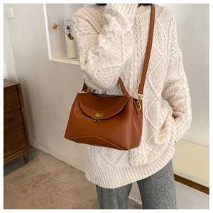 Detailed view of brown leather trapezoid bag with gold metal buckle and top handle strap