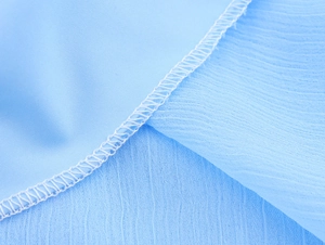 Detailed close-up of light blue chiffon fabric texture and white stitched seam finishing