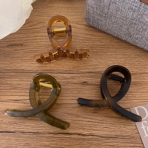 Three elegant translucent hair claws in amber, dark green, and brown on a wood surface