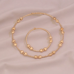 Vista piana del set collana e bracciale con perline a cuore dorate su tessuto morbido