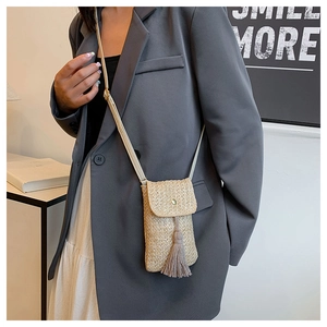 Detail of beige woven straw phone bag with tassel and leather strap on model