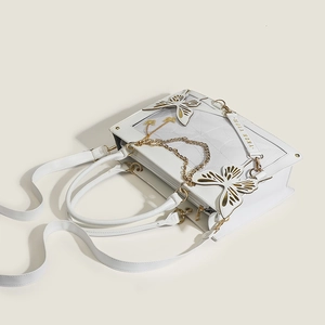 Detail of white butterfly ita bag with golden hollow charms and branded logo strap