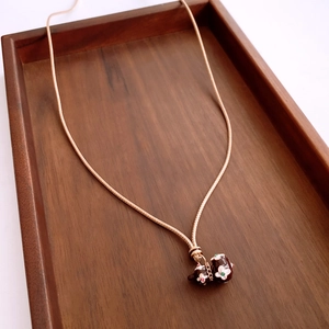 Detail of a gold snake chain necklace with brown enamel flower beads on a wood tray