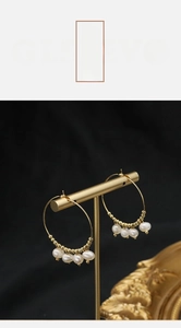 Detail of gold-plated hoop earrings with hanging pearls on a luxury display stand