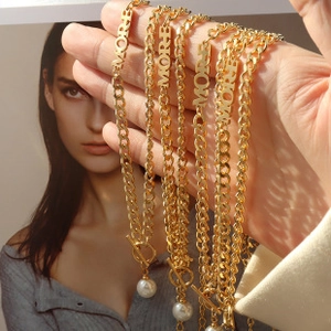 Detailed view of gold chain necklaces featuring MORE letter charms and pearl T-bar clasps