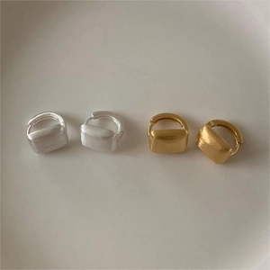 Close-up of square brushed metal earrings in gold and silver finishes on a beige background