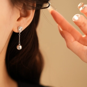 Detailed view of silver drop earring with pear-cut crystal and gray pearl on a model