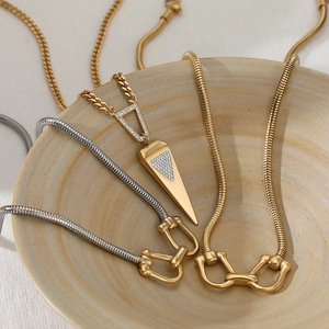 Layered gold geometric triangle and horsebit pendant necklaces on a ceramic bowl