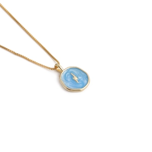 Detail of gold box chain necklace with a blue enamel heart pendant and lightning bolt