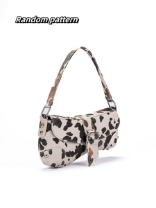 Asymmetric shoulder bag featuring cow print pattern and metal rivet details on white background