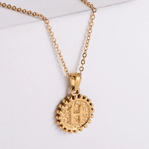 Detail of 18k gold plated hammered disc pendant featuring letter H on white steps