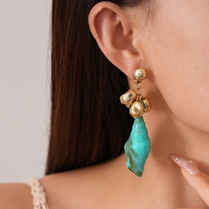 Detailed view of turquoise conch-shaped pendant earring on model for beach style
