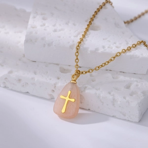 Close-up of golden cross pendant with pink teardrop stone on white stone background