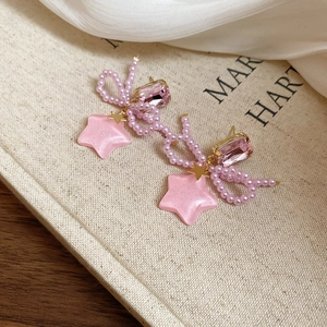 Detail of pink bow and star earrings with faux crystals and golden accents on fabric