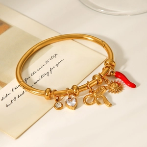 Detailed shot of golden stainless steel bangle with sun, bow, and red chili pepper charms