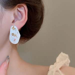 Gros plan de boucles d'oreilles fleur en nacre avec papillons dorés portées par le modèle