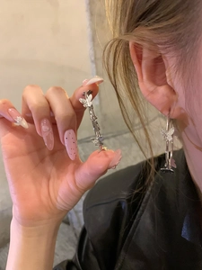 Detail of silver hoop earrings with pavé-set butterfly charms on a grey background
