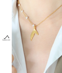 Close-up of golden mermaid tail pendant on a stainless steel pearl necklace on neck