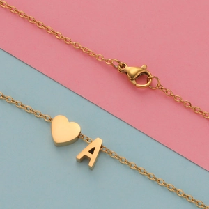 Detail of gold heart and letter A pendant necklace on pink and blue background