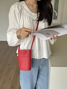 Minimalist red cylindrical crossbody mini bag with litchi texture on white shirt background