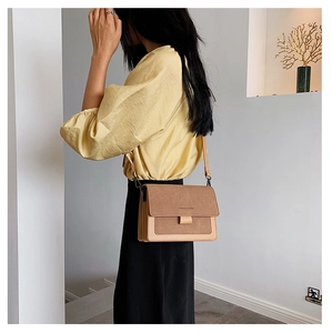 Close-up of brown suede and leather crossbody square bag with a brand logo on the flap